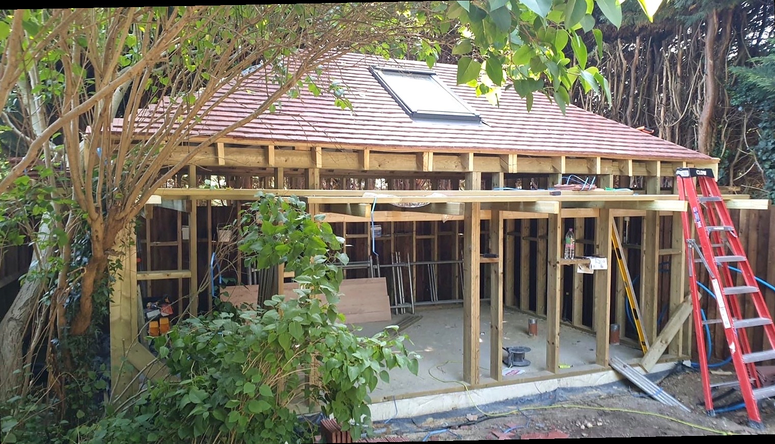 Timber-frame garden room under construction in a wooded garden