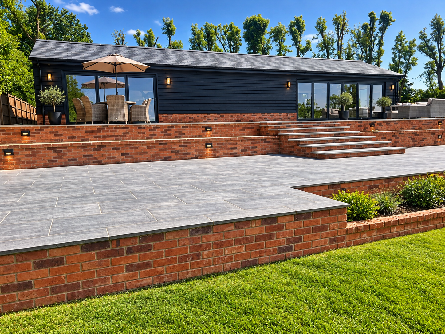 Garden terrace construction with porcelain paving, brick retaining walls, steps and a black timber garden building