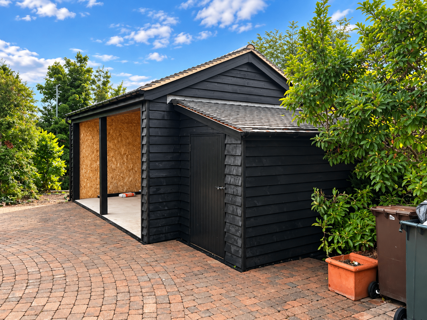 Curved brick-paved driveway beside a black garden building during construction