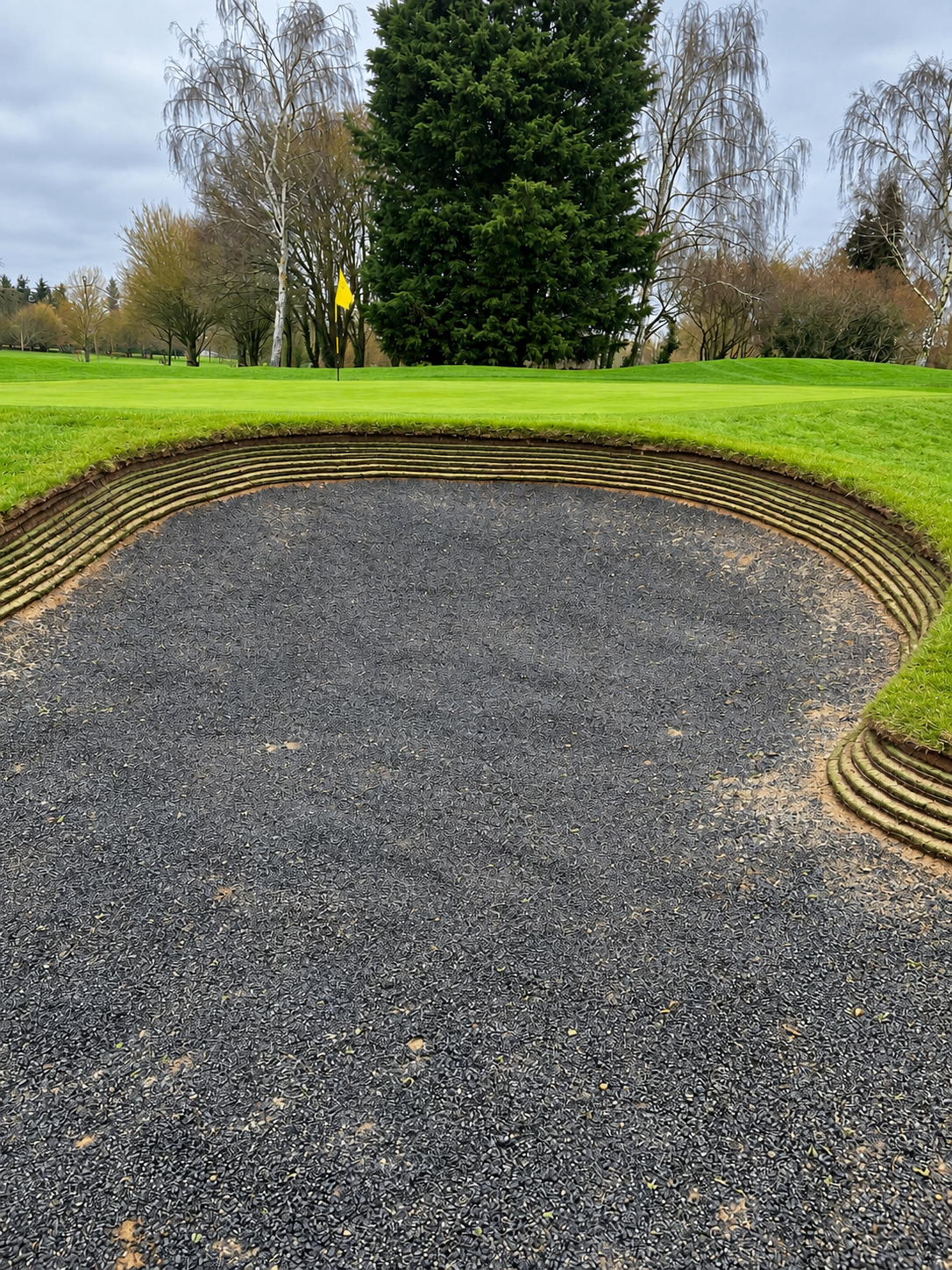 Golf bunker with layered revetted turf face, fine gravel base, green and flag beyond