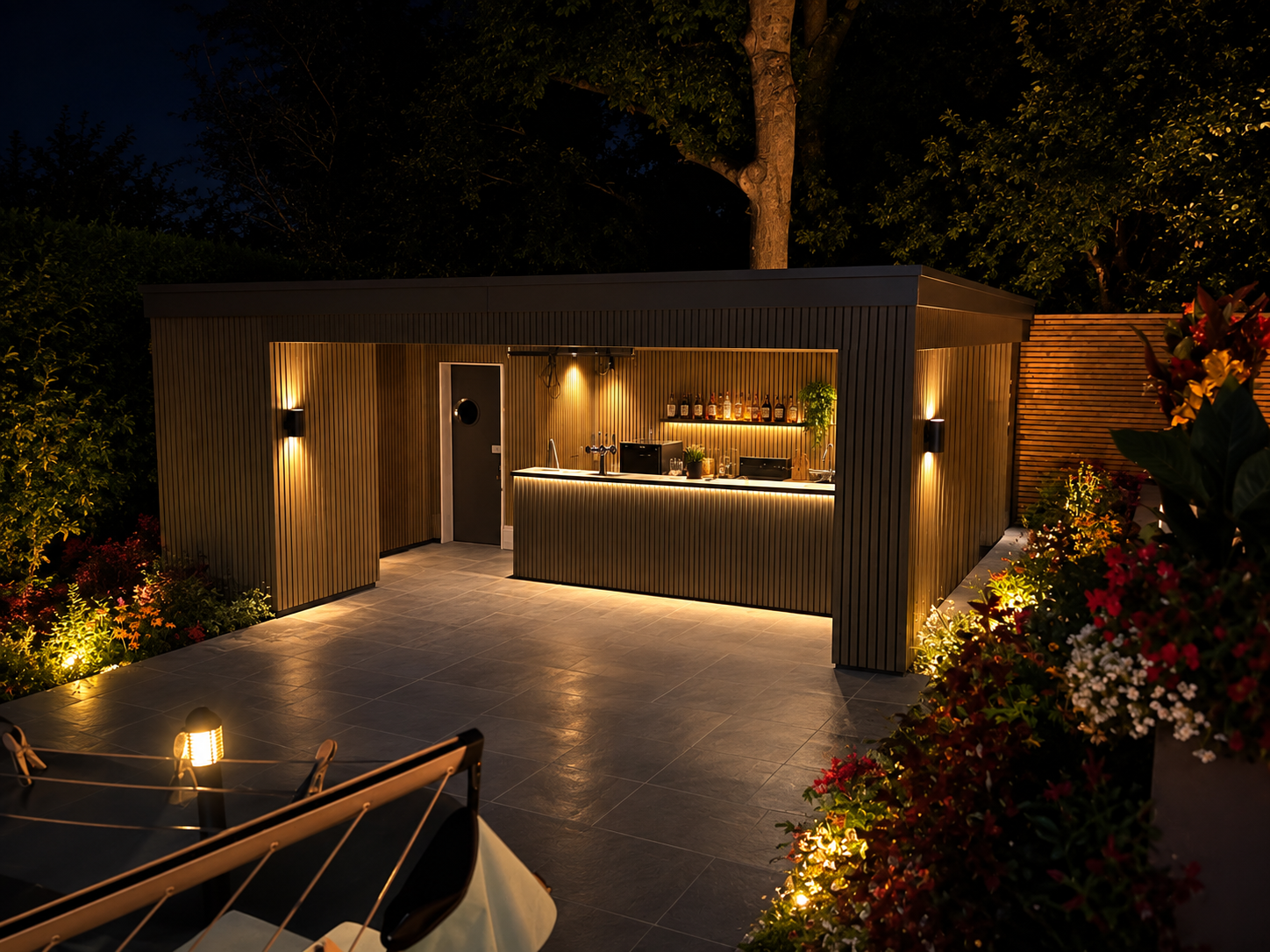 Illuminated garden building with a fitted outdoor bar, paved entertaining terrace and surrounding planting